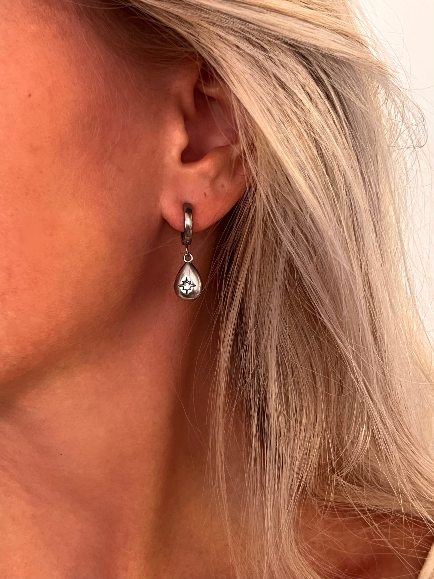 Close-up of a person's ear wearing the Aeva polished stainless steel star drop earrings.