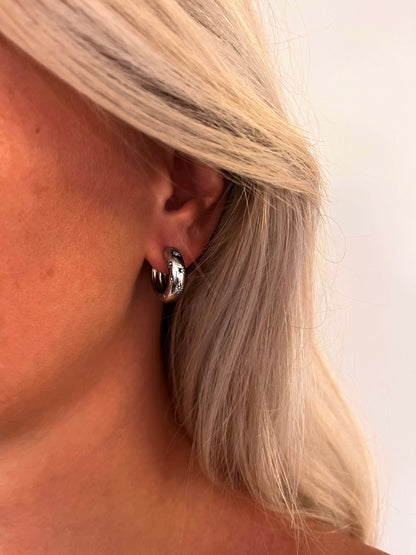 Close-up of the Aeva polished stainless steel hoop earrings with a sculptural celestial design.