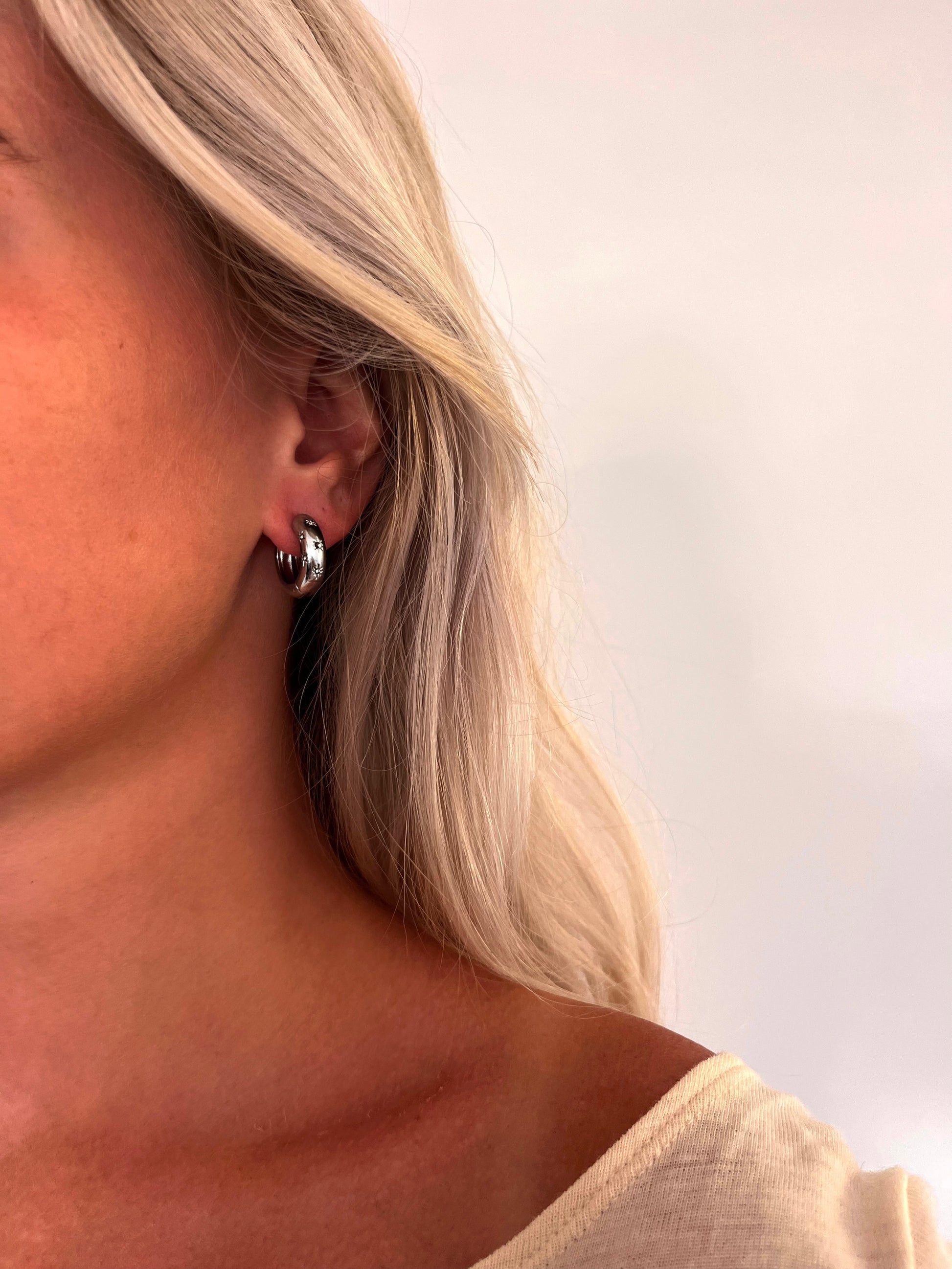 A person wearing the Aeva celestial hoop earrings in polished stainless steel.
