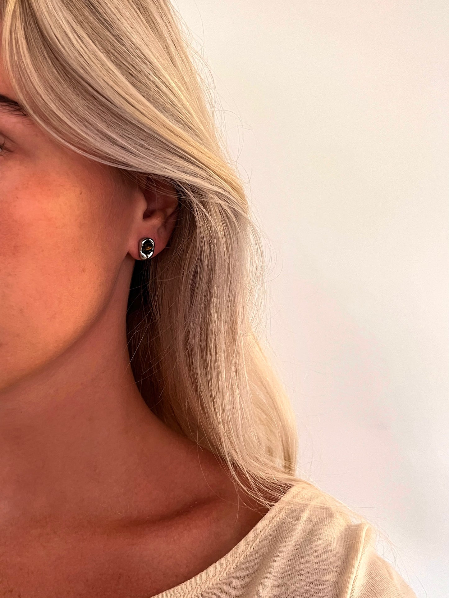 A person wearing the Auris tiger's eye stud earrings in polished stainless steel.