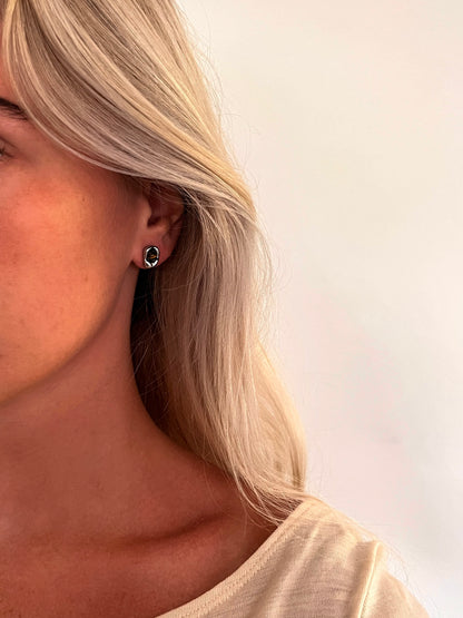 A person wearing the Auris tiger's eye stud earrings in polished stainless steel.