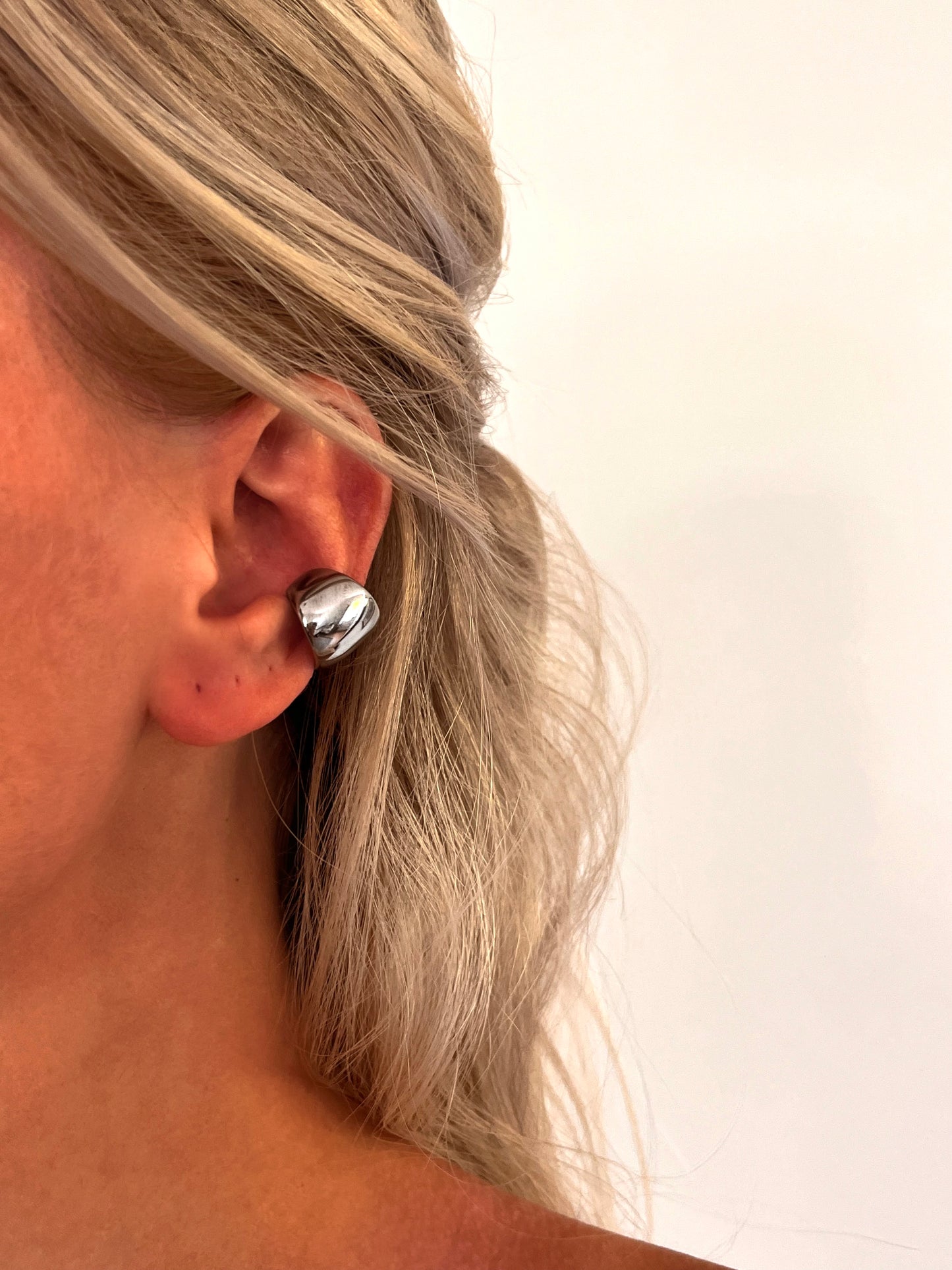 Close-up of the Cova sculptural dome ear cuff in polished stainless steel with a smooth rounded design.