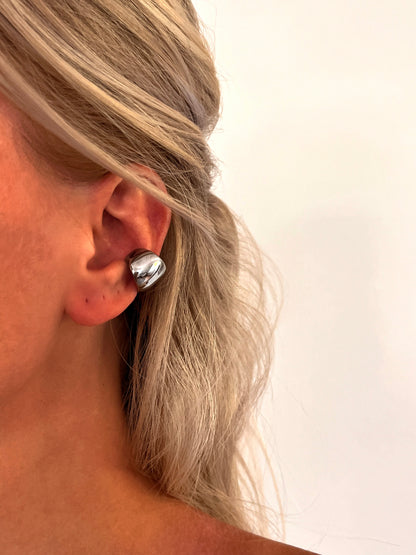 Close-up of the Cova sculptural dome ear cuff in polished stainless steel with a smooth rounded design.