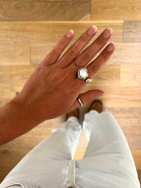 A hand wearing the Cove freshwater pearl ring in polished stainless steel, photographed from above with white denim and brown boots in the background.