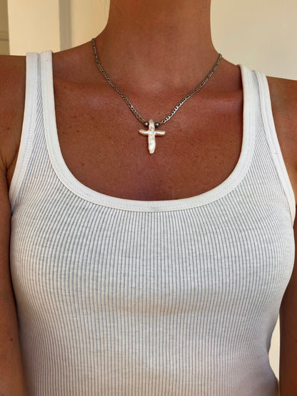 A close-up of a person wearing the crux necklace a silver cross freshwater pendant necklace on a silver chain, paired with a white ribbed tank top.