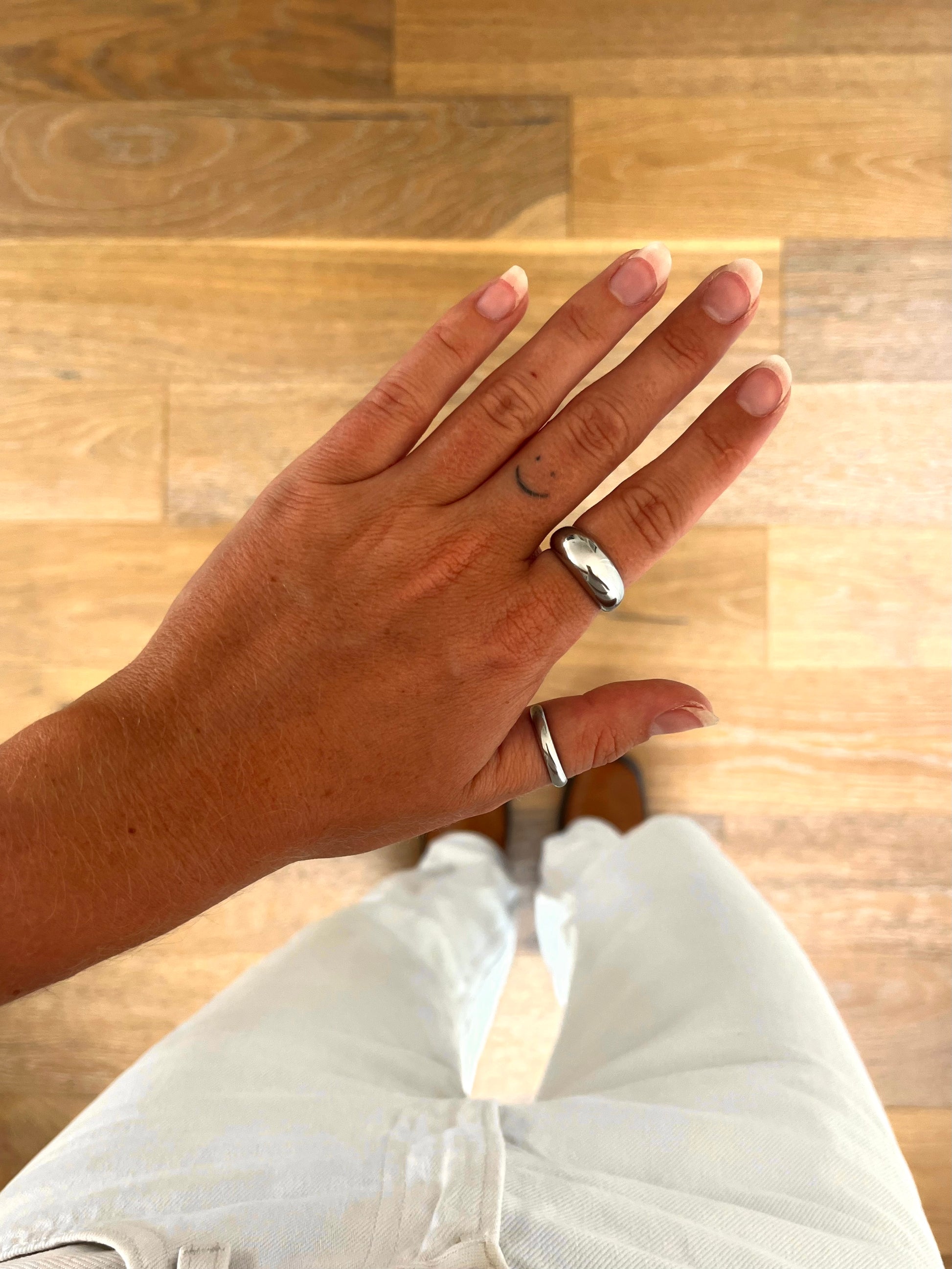 A hand wearing the Dome I sculptural dome ring in polished stainless steel, photographed from above with white denim and brown boots in the background.