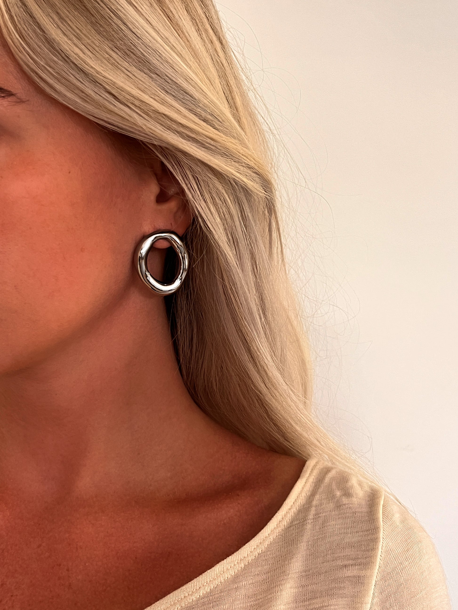 A person wearing the Domena sculptural oval hoop earrings in polished stainless steel.