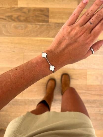 A wrist wearing the Fora I four-leaf clover bracelet in polished stainless steel, photographed from above with a beige skirt and brown boots in the background.
