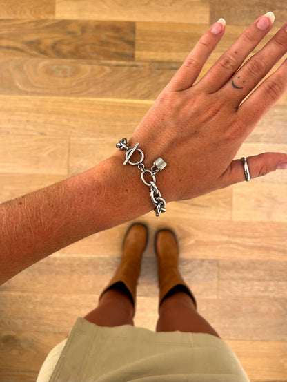 A wrist wearing the Locke sculptural chain bracelet in polished stainless steel from another angle, photographed from above with a beige skirt and brown boots in the background.
