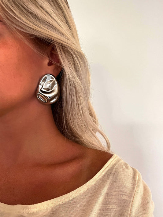 A person wearing the Melo sculptural stud earrings in polished stainless steel.