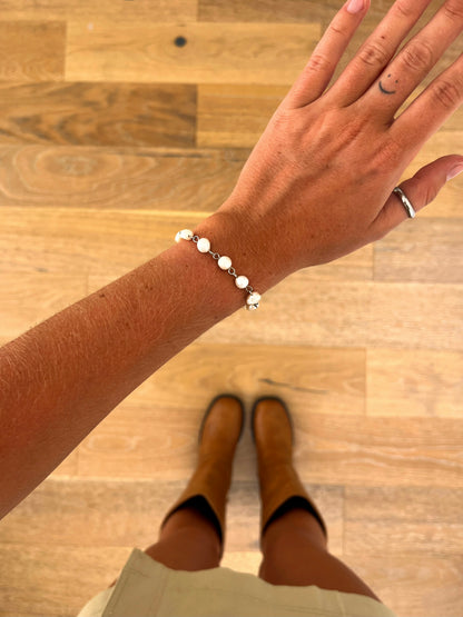 A wrist wearing the Nerine freshwater pearl bracelet in polished stainless steel, photographed from above with a beige skirt and brown boots in the background.