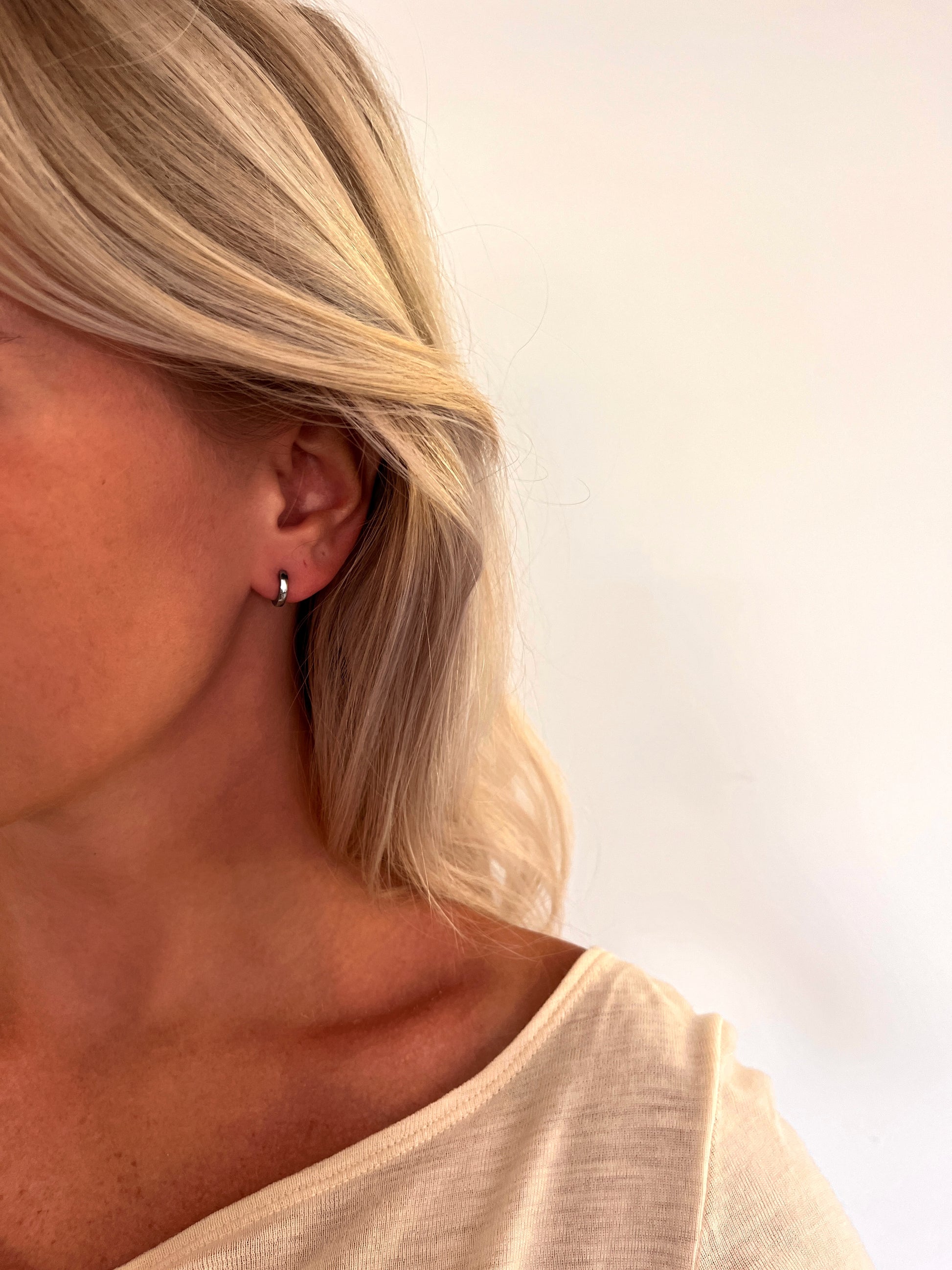 A person wearing the Orbis polished stainless steel hoop earrings with a rounded sculptural design.