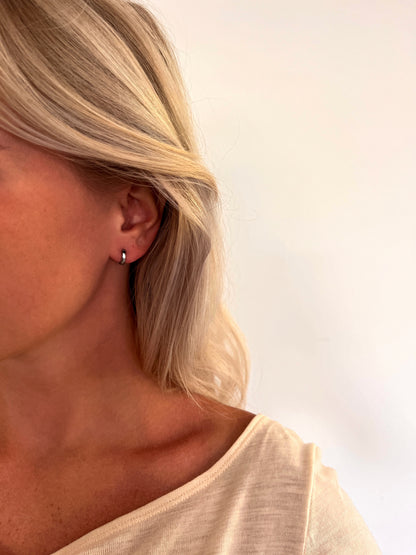 A person wearing the Orbis polished stainless steel hoop earrings with a rounded sculptural design.