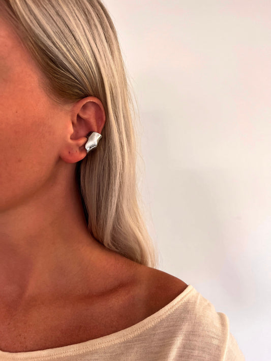 A person wearing the Plica folded sculptural ear cuff in polished stainless steel.
