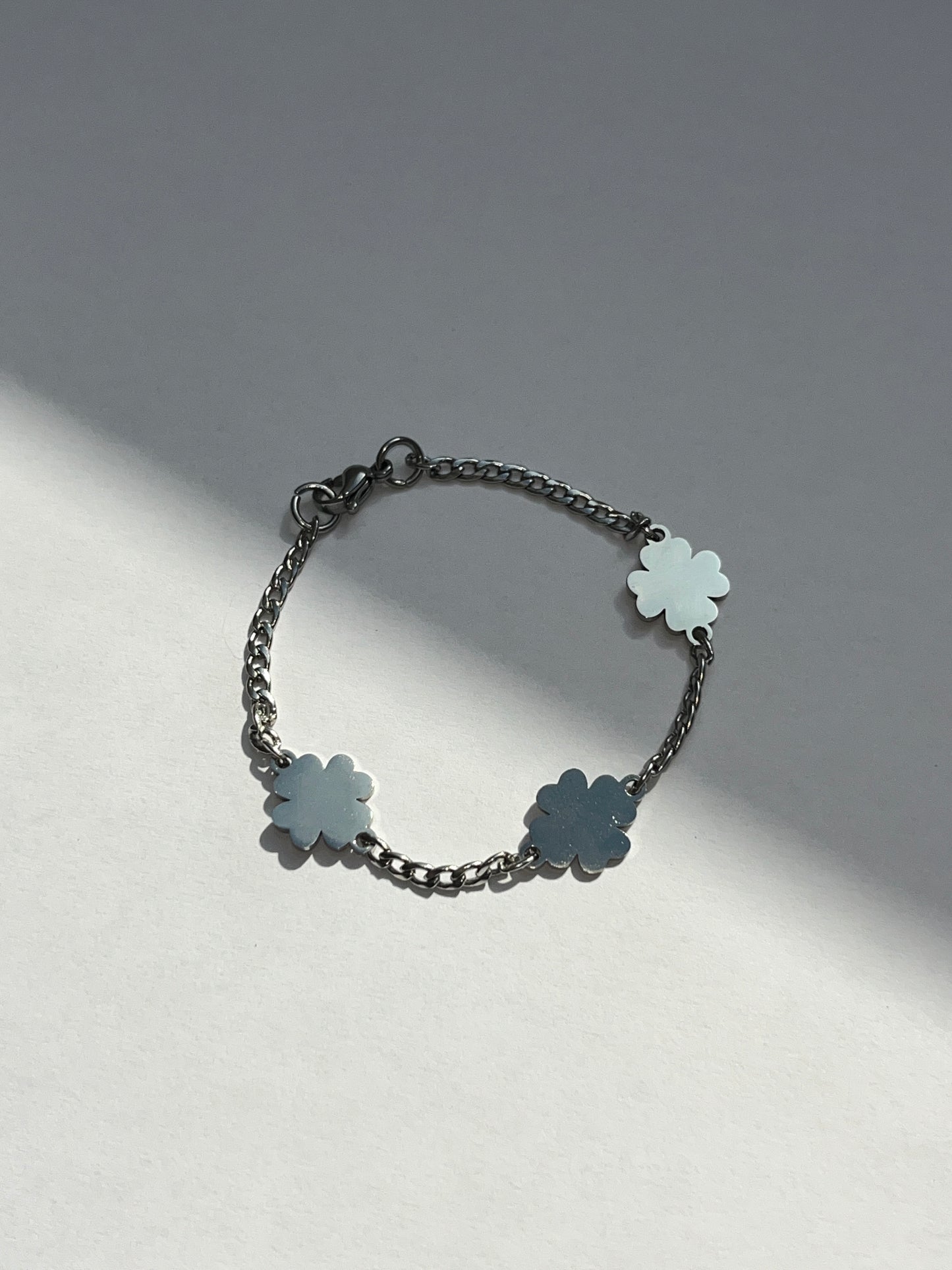 A silver stainless steel bracelet featuring a slim chain with three four-leaf clover charms on a light background.