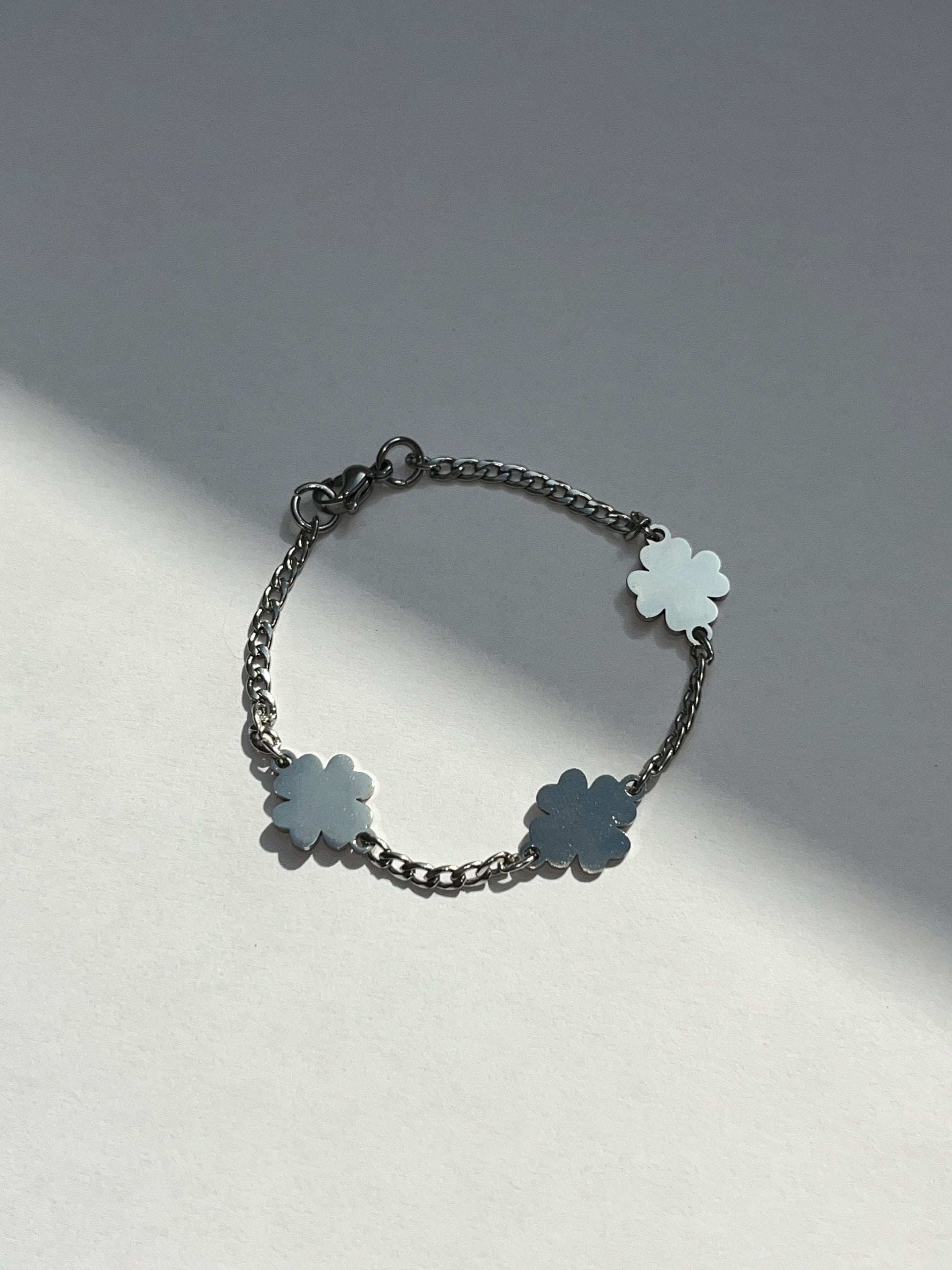 A silver stainless steel bracelet featuring a slim chain with three four-leaf clover charms on a light background.