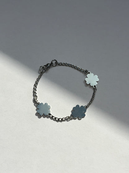 A silver stainless steel bracelet featuring a slim chain with three four-leaf clover charms on a light background.