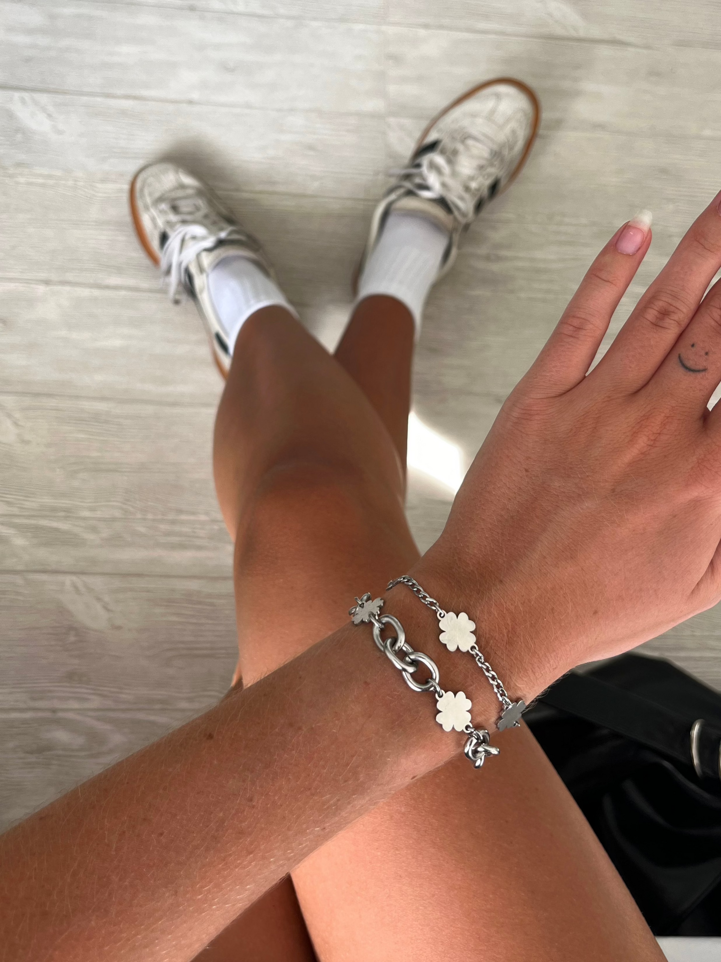 A model's wrist wearing a silver- and stainless steel-colored bracelet with four-leaf clover charms on a chunky chain.
