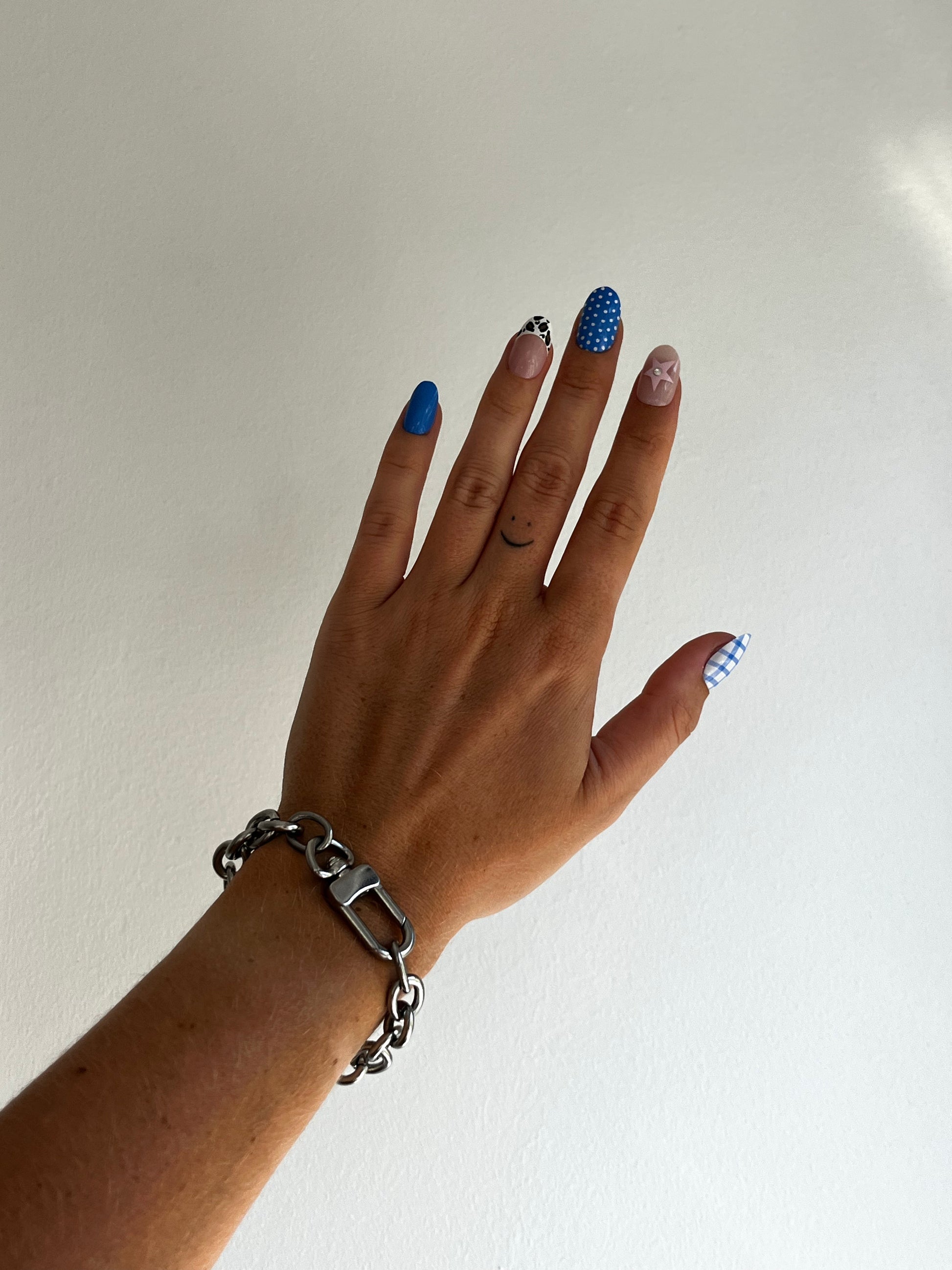 Hand wearing a unisex silver stainless steel chain bracelet with blue nail polish on a plain white bright background