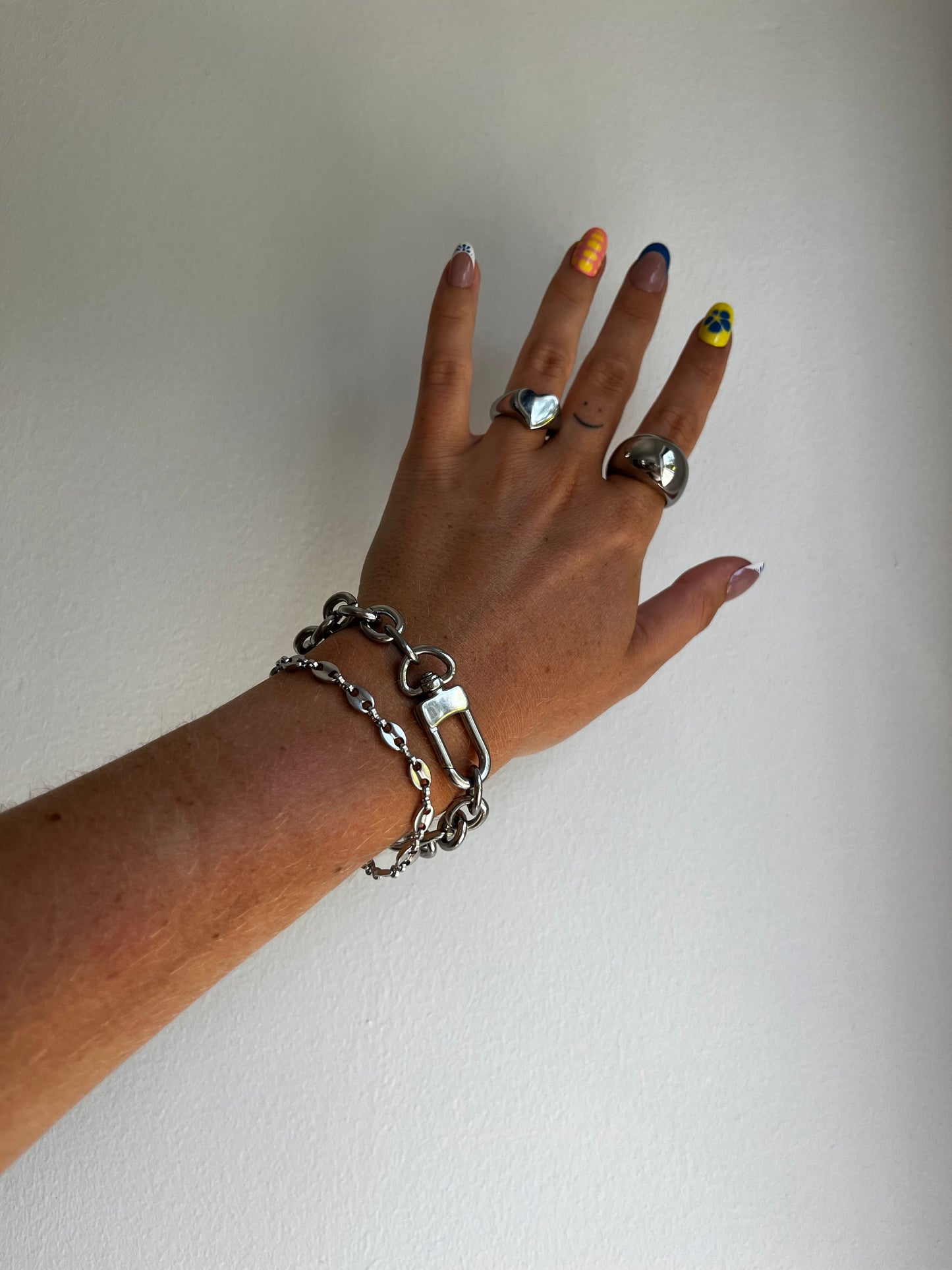 Hand wearing multiple silver stainless steel karliekarlo rings and bracelets on a plain background and focusing on the grand clasp bracelet