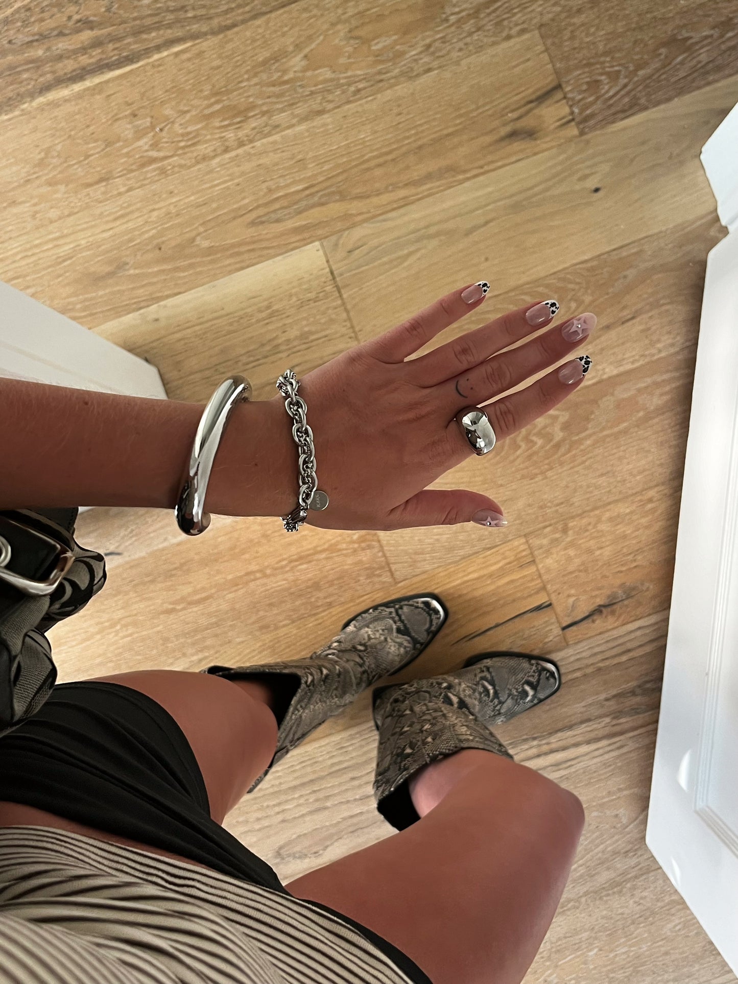 Unisex silver stainless steel intertwined bracelet stacked with bangle and dome ring on finger.