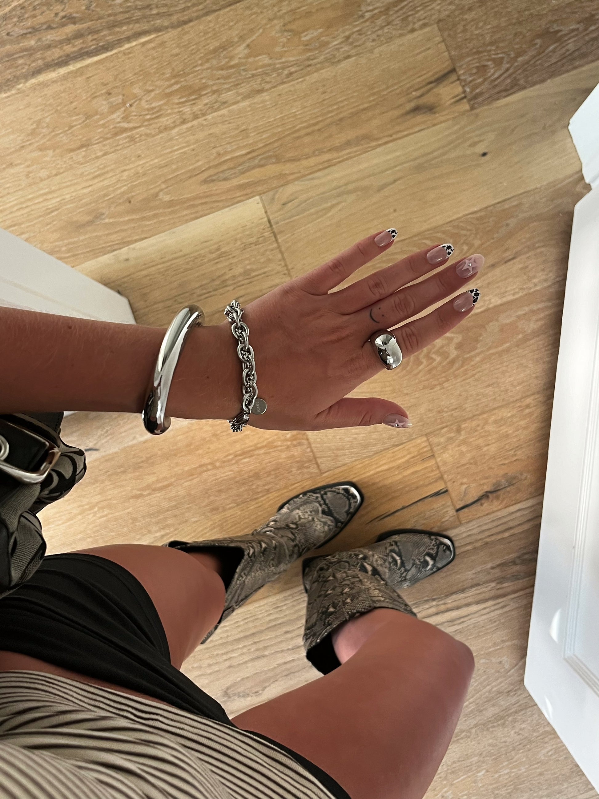 Unisex silver stainless steel intertwined bracelet stacked with bangle and dome ring on finger.