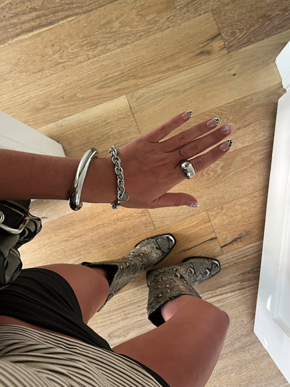 Unisex silver stainless steel intertwined bracelet stacked with bangle and dome ring on finger.