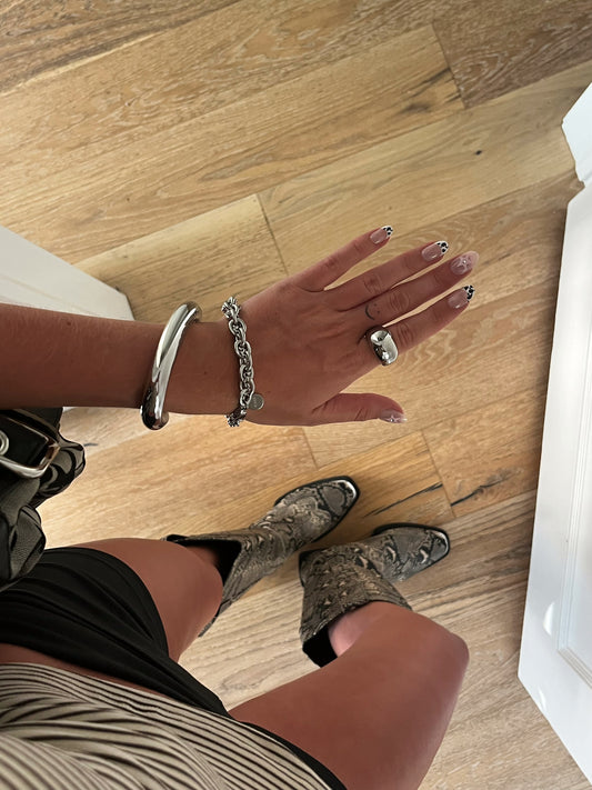 Unisex silver stainless steel intertwined bracelet stacked with bangle and dome ring on finger.