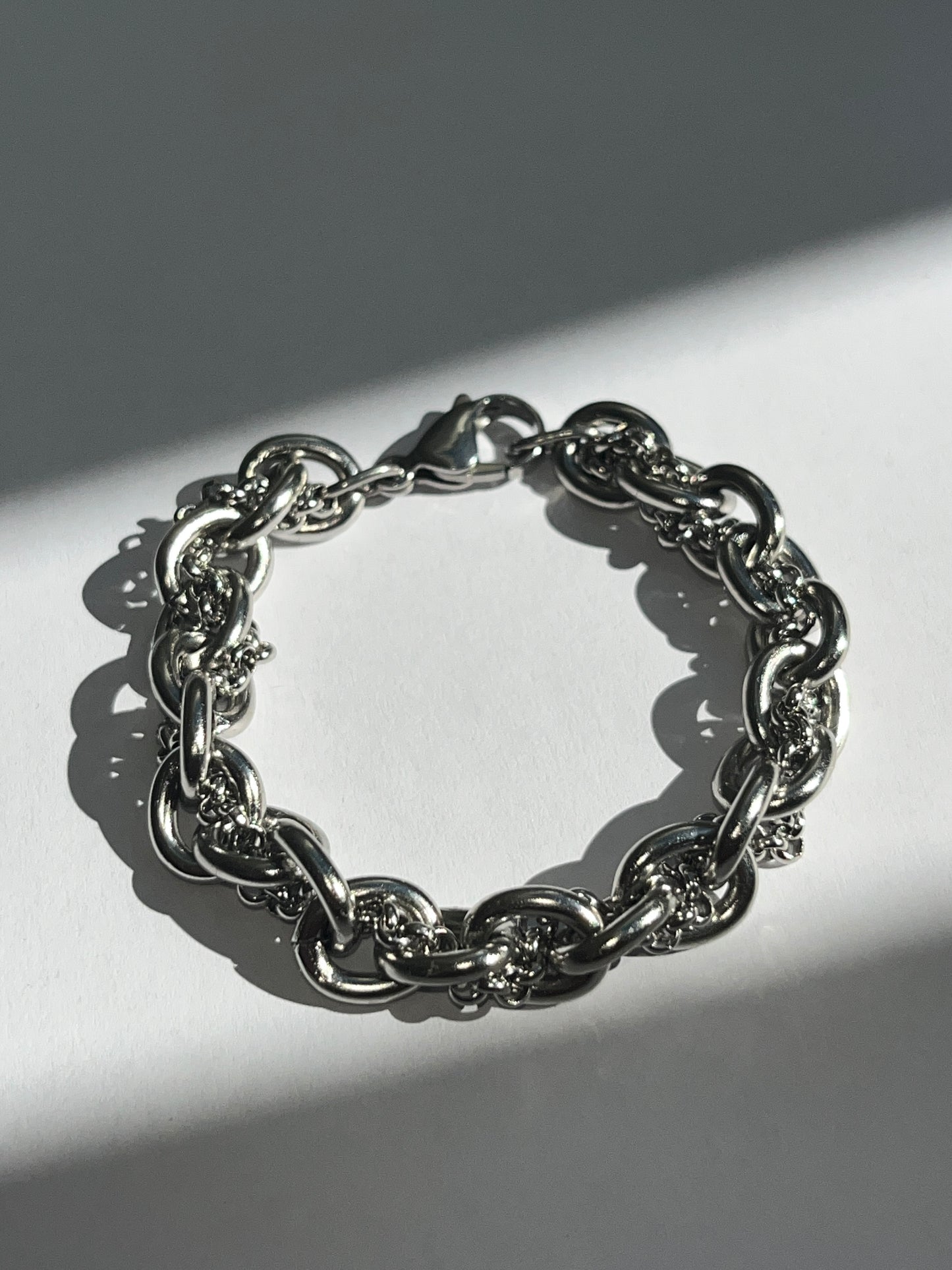 Closeup product image of chunky silver stainless steel intertwined chain bracelet showing texture and links.