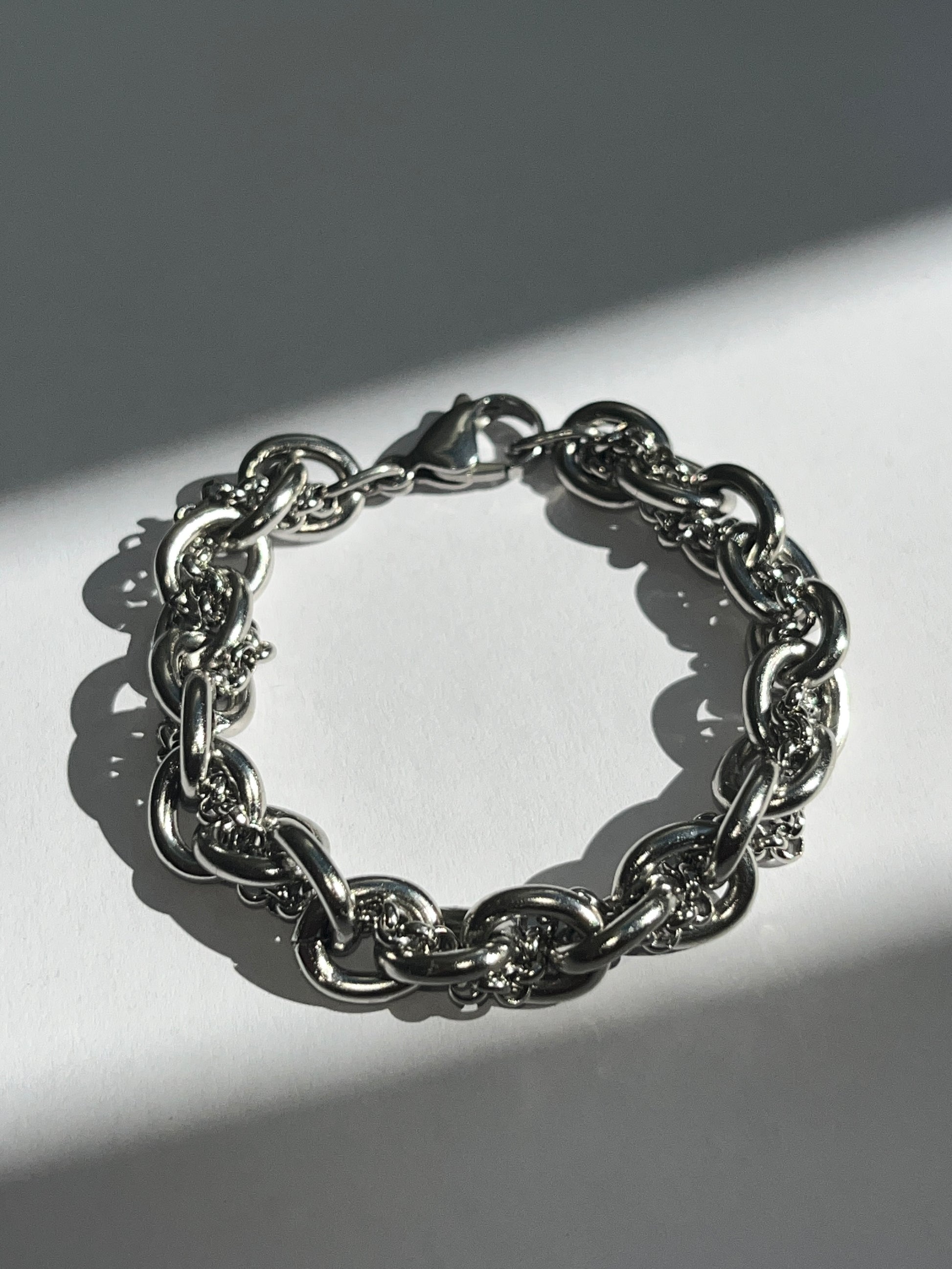 Closeup product image of chunky silver stainless steel intertwined chain bracelet showing texture and links.
