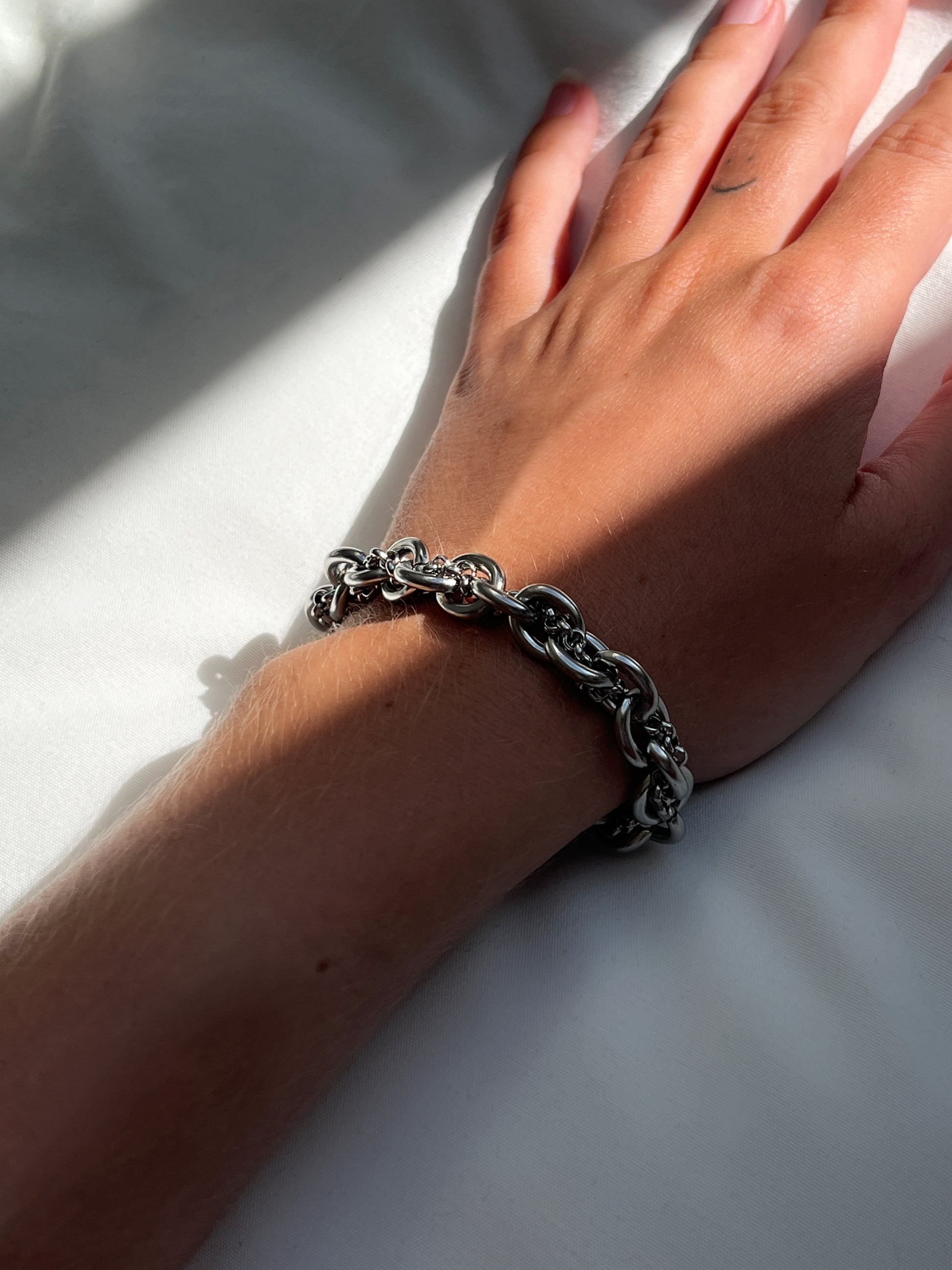 Closeup of chunky silver stainless steel intertwined chain bracelet showing texture and links.