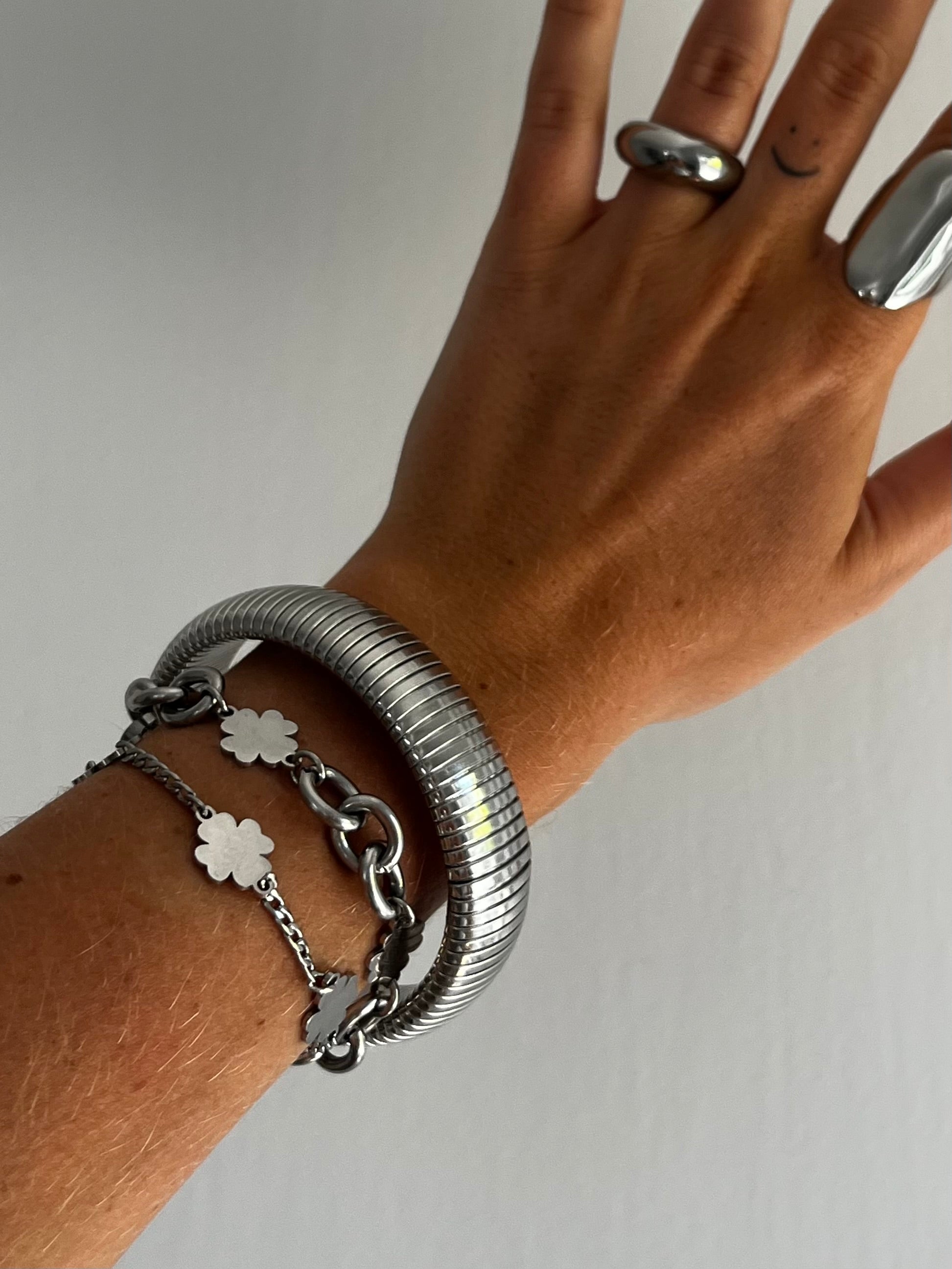 Closeup of THE SPRING BANGLE highlighting coiled flexible stainless steel design, high-polish unisex bracelet.