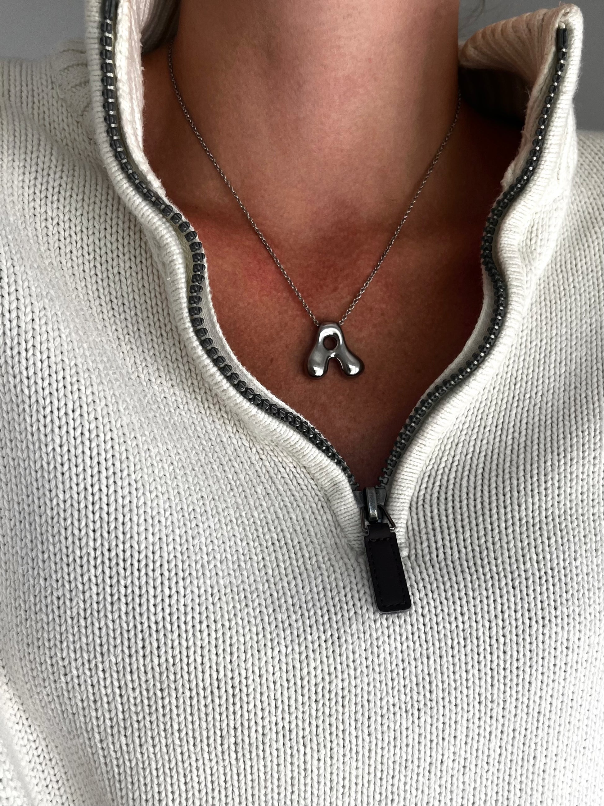 Necklace with a pendant worn by a person in a light gray sweater.