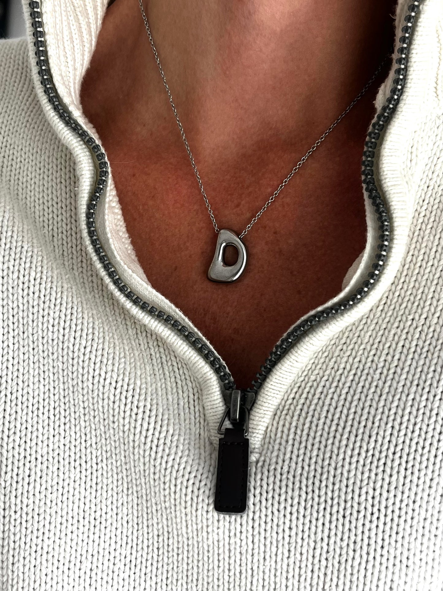 Necklace with a unique pendant worn by a person wearing a light gray sweater.