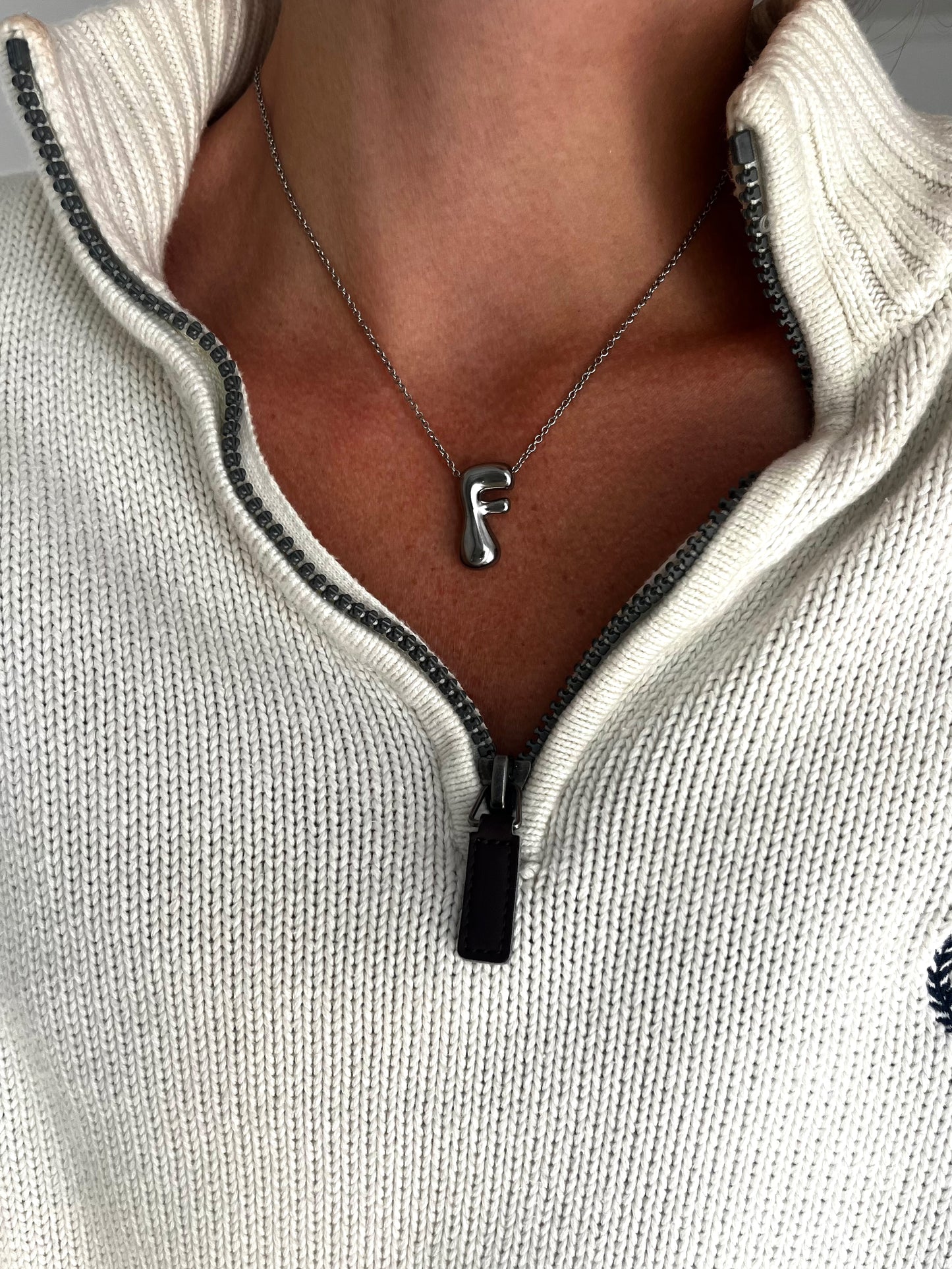 Necklace with a letter 'F' pendant worn by a person in a white sweater.