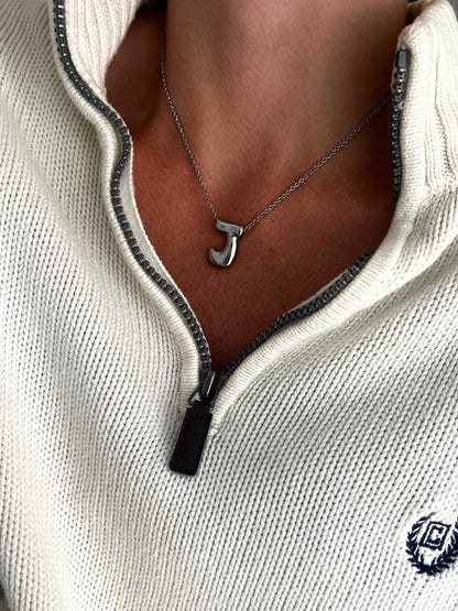 Necklace with a 'J' pendant worn by a person in a white sweater.