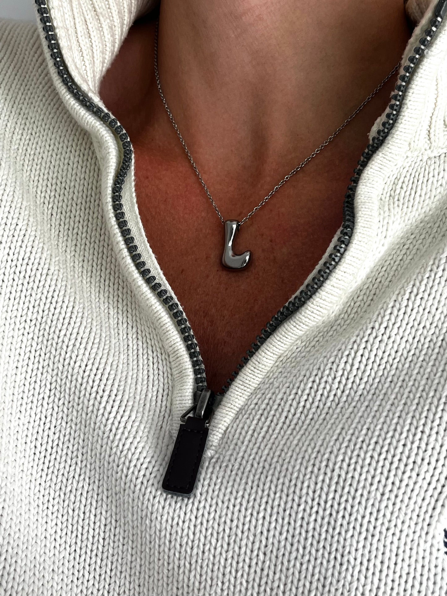 Necklace with a letter 'L' pendant worn by a person in a light-colored sweater.