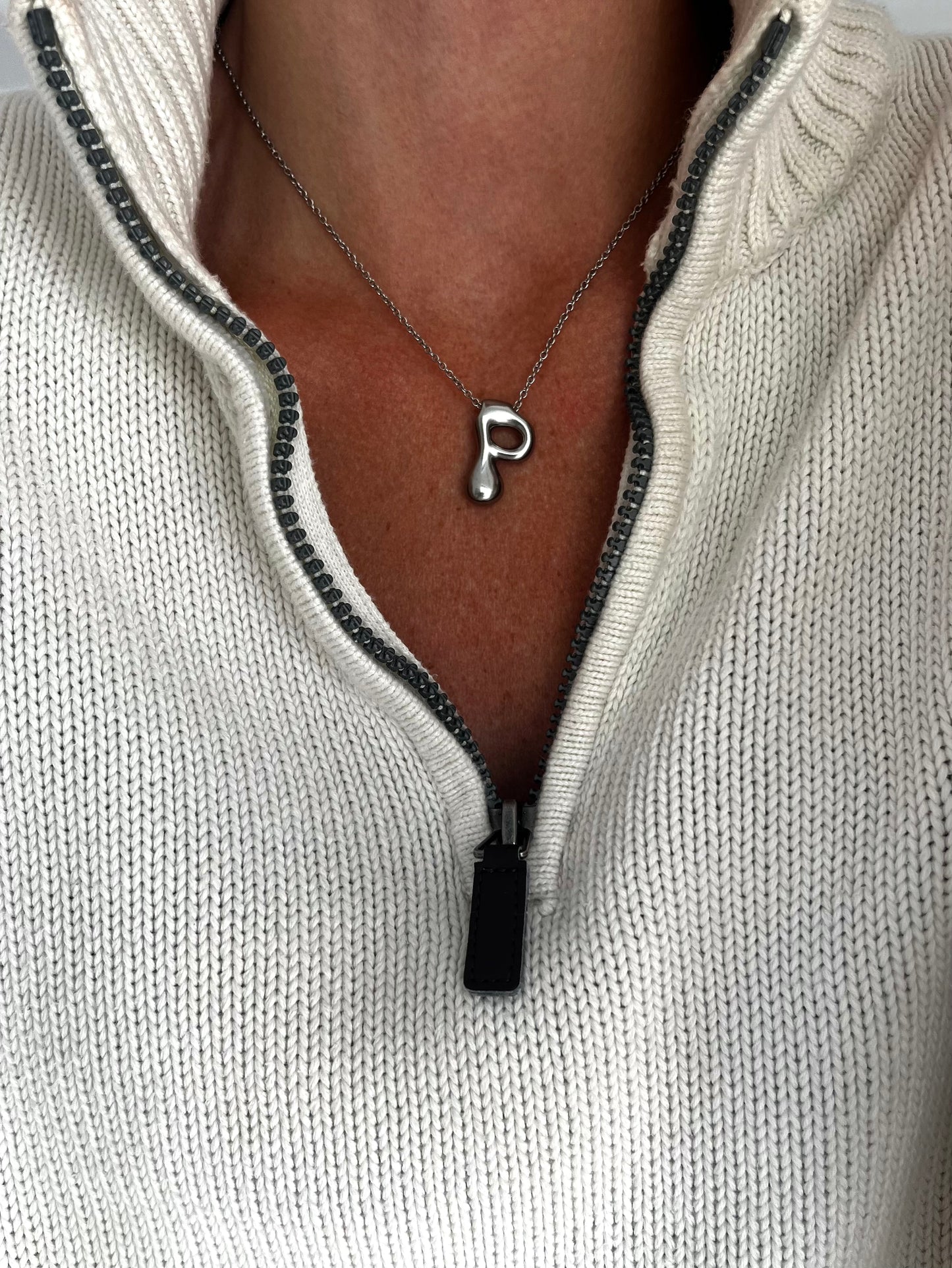 Necklace with a letter 'P' pendant worn by a person in a light gray sweater.