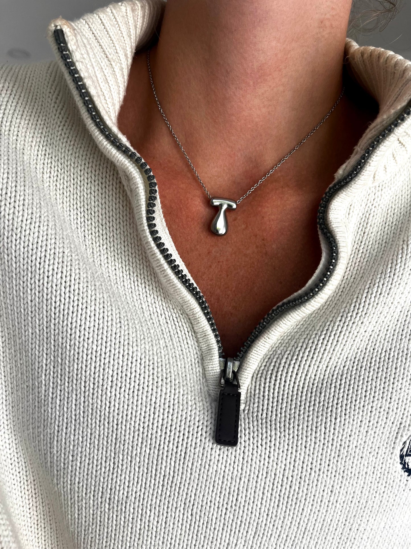 Necklace with a pendant worn by a person in a light gray sweater.