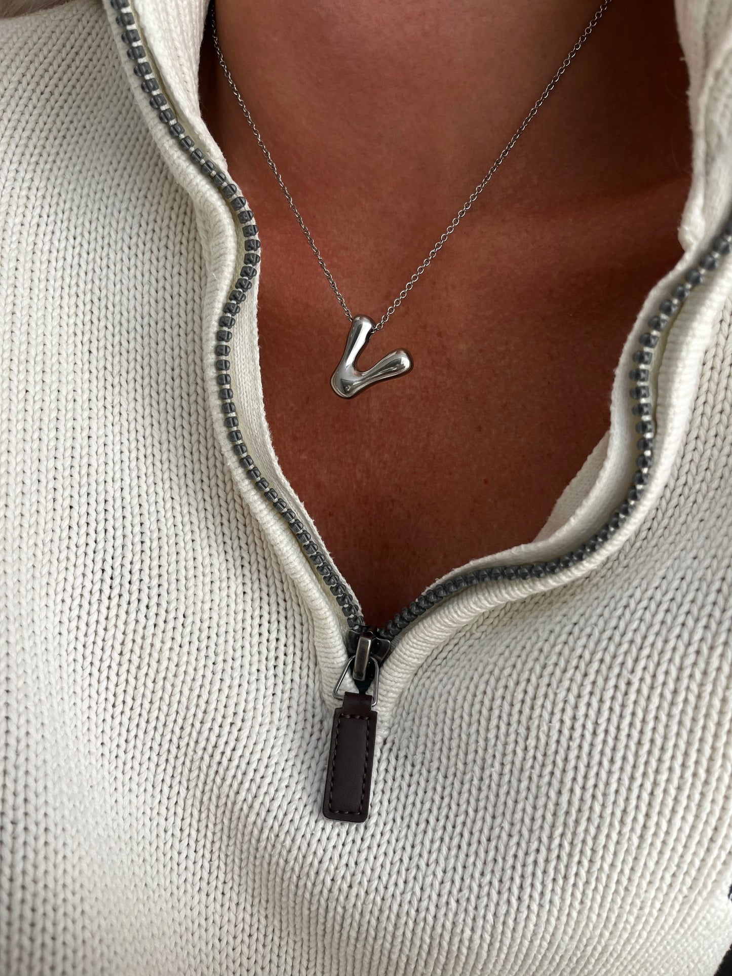 Necklace with a unique pendant worn by a person in a light gray zip-up sweater.