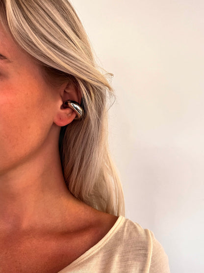 A person wearing the Voluta spiral sculptural ear cuff in polished stainless steel.