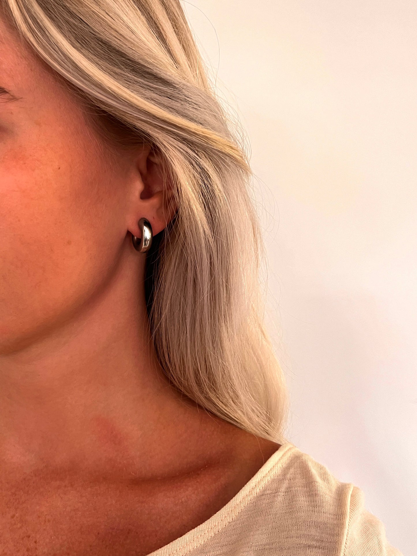 A person wearing the Voluta I sculptural hoop earrings in polished stainless steel.