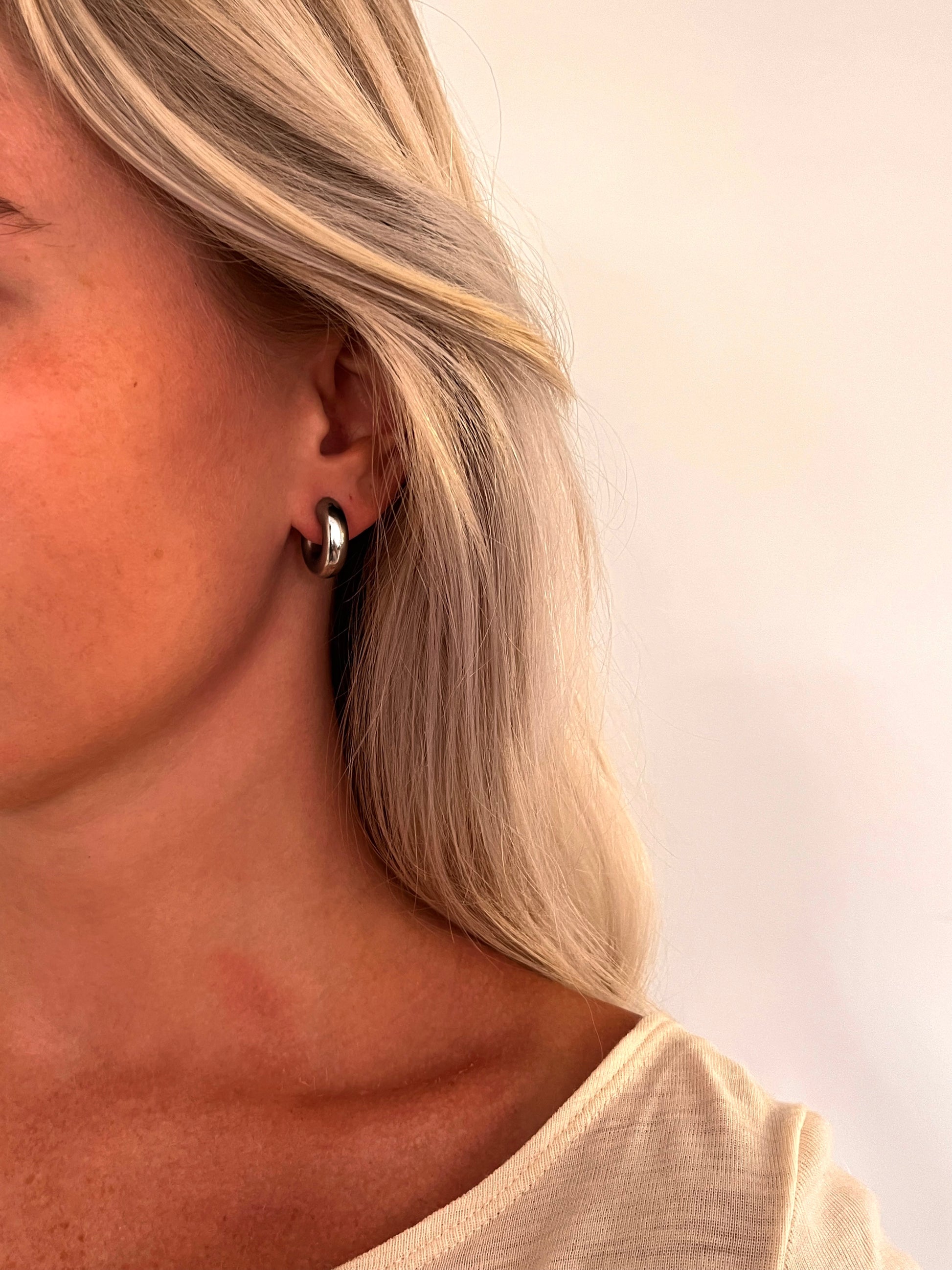 A person wearing the Voluta I sculptural hoop earrings in polished stainless steel.