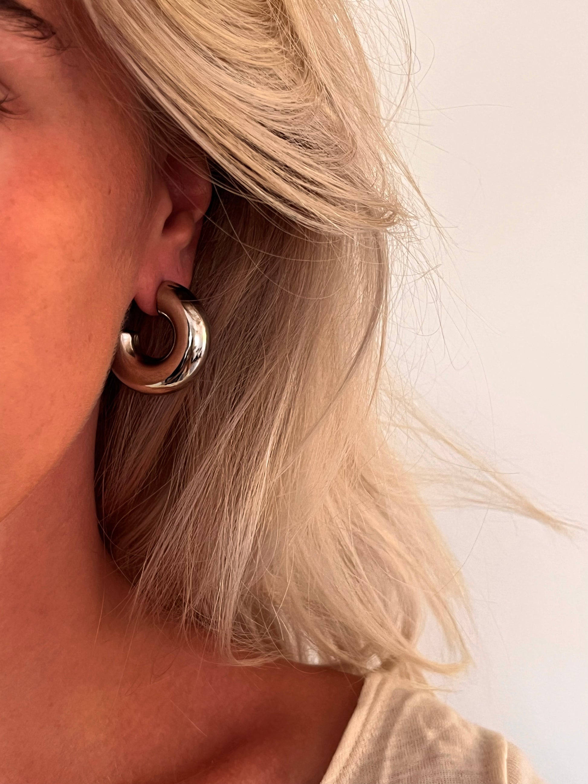 Close-up of the Voluta II polished stainless steel sculptural hoop earrings with a bold curved silhouette.
