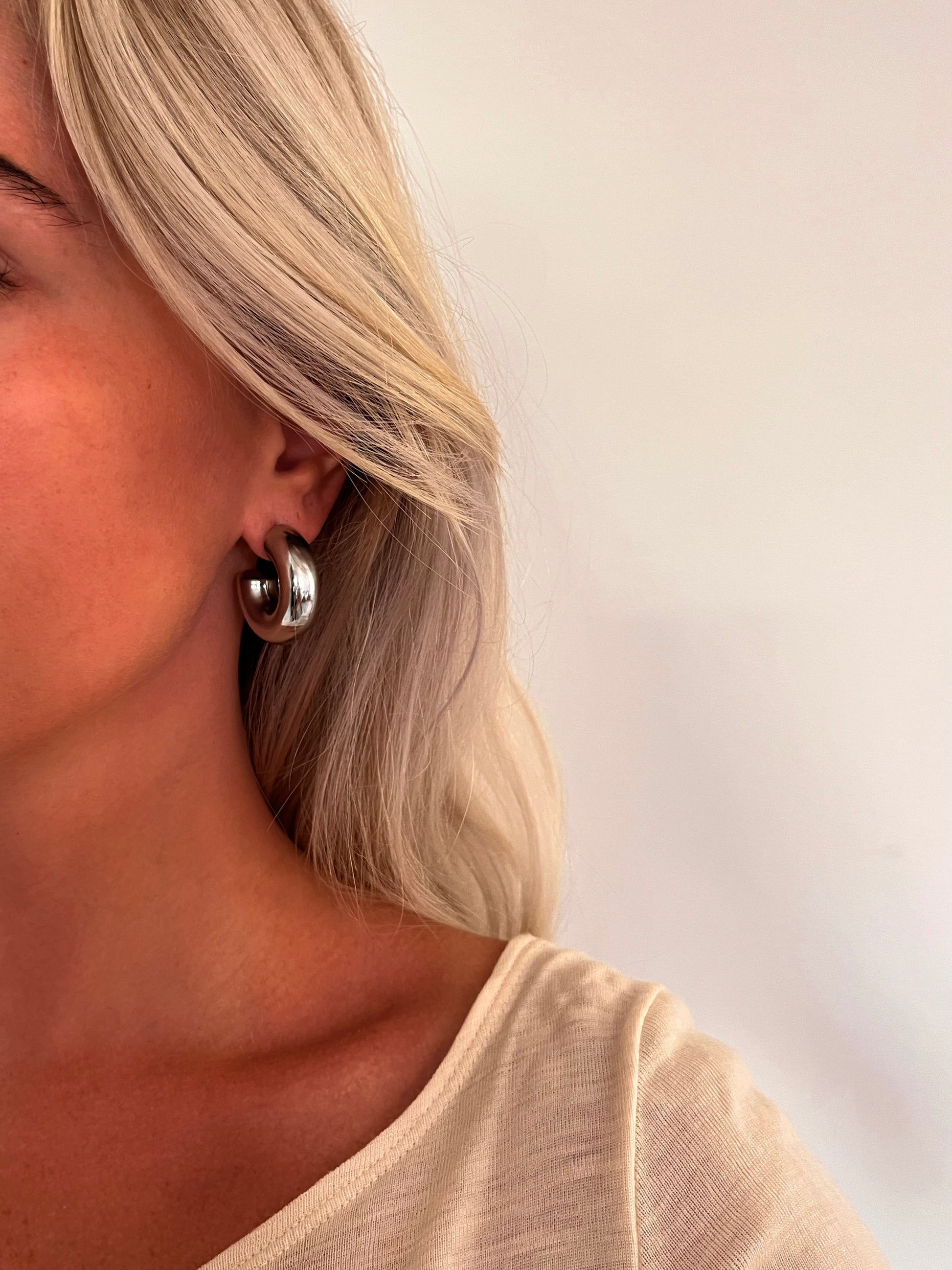 A person wearing the Voluta II bold sculptural hoop earrings in polished stainless steel.