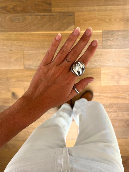 A hand wearing the Whorl sculptural engraved ring in polished stainless steel, photographed from above with white denim and brown boots in the background.